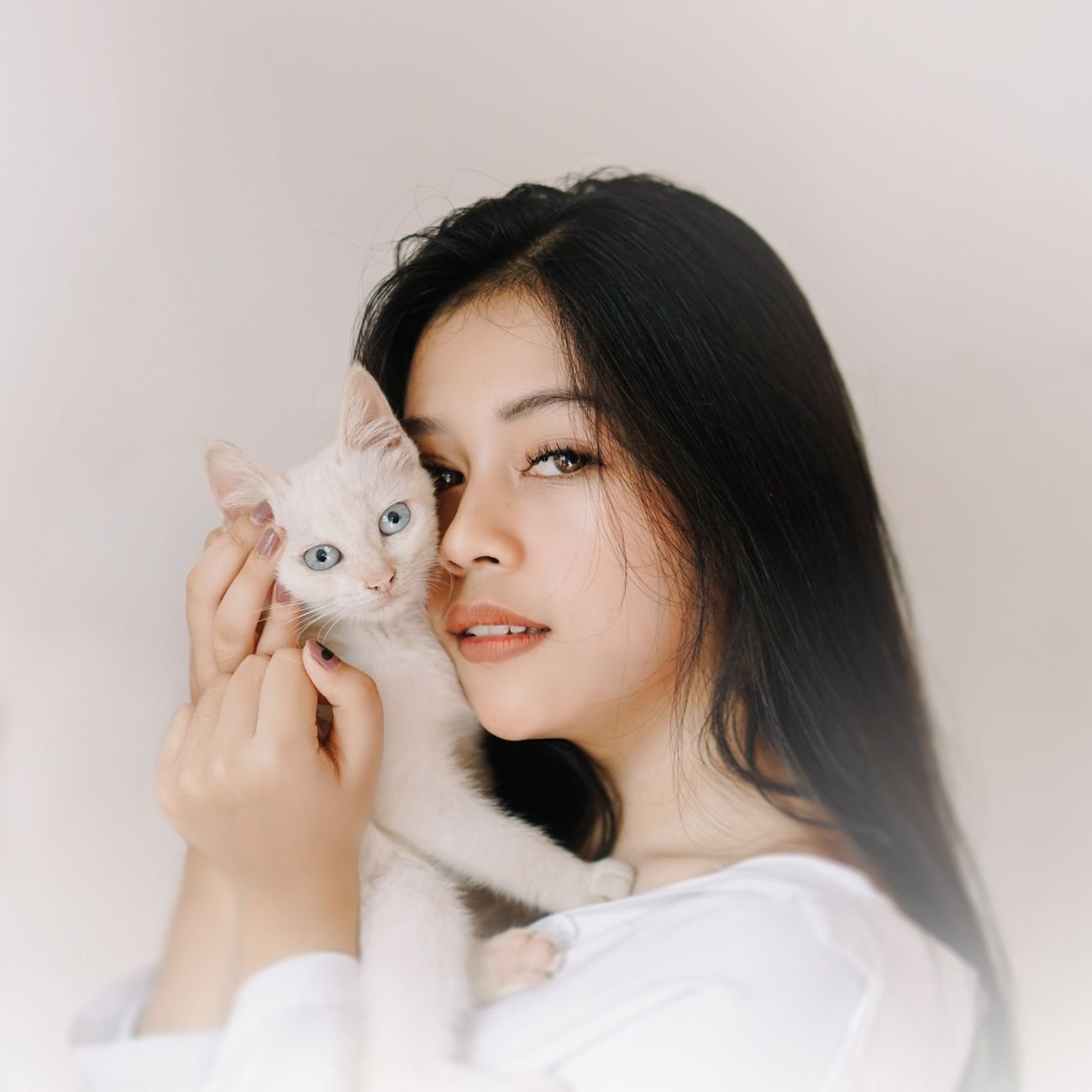 Warm portrait of woman lovingly holding a white kitten with blue eyes indoors.